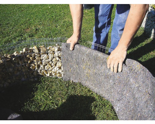 Persoon bevestigt scheidingsvlies aan een schanskorf in de tuin.