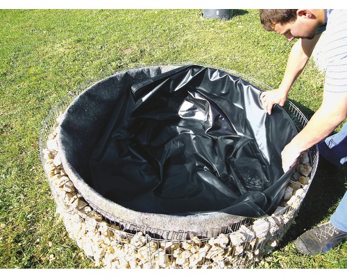 Een man legt vijverfolie in een ronde, met stenen gevulde schanskorf