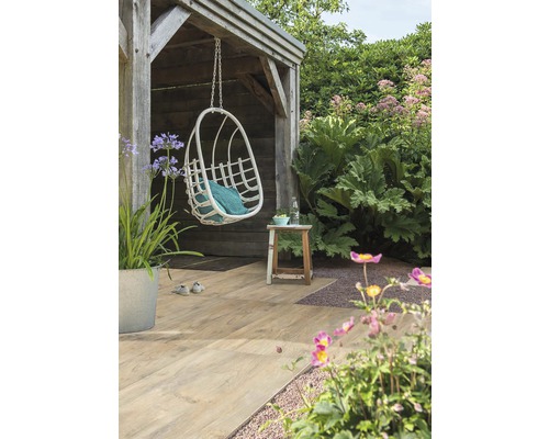 Tuinlandschap met hangende mandstoel, houten vloer en weelderige beplanting.