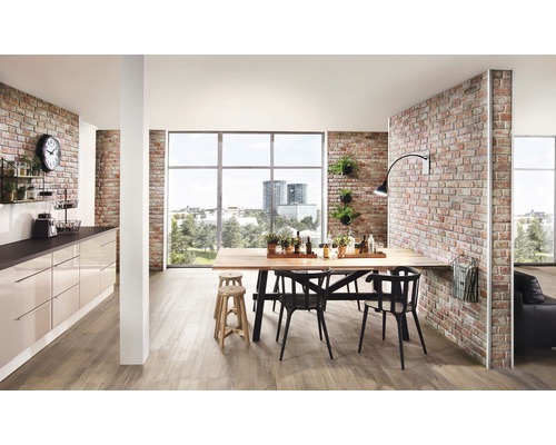 Lichte woonkamer met eettafel, stoelen, kitchenette en bakstenen muur