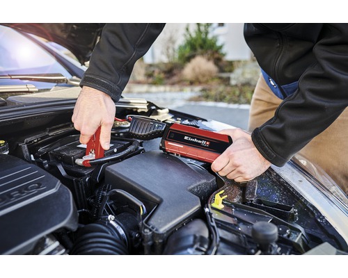 Een man sluit een autobatterij aan met een rode jumpstarter van Einhell.