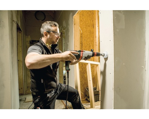 Een man boort met een boormachine een gat in een muur op een bouwplaats.