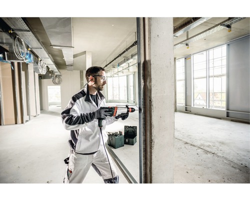 Een man boort met een klopboormachine een gat in een betonnen muur in een ruwbouw