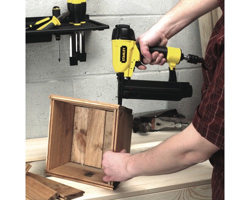 Iemand gebruikt een Stanley tacker om een houten kist in elkaar te zetten.