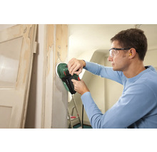 Een man schuurt een deurkozijn met een excentrische schuurmachine.