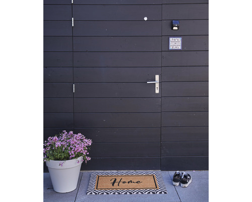 Entree met deurmat, bloempot en pantoffels voor een houten deur.