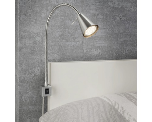 Een flexibele, zilverkleurige LED-bedlamp is bevestigd aan een wit bedframe.