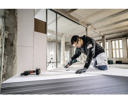 Een vakman snijdt een gipsplaat met speciaal gereedschap in een casco, waarbij ander gereedschap klaar ligt.