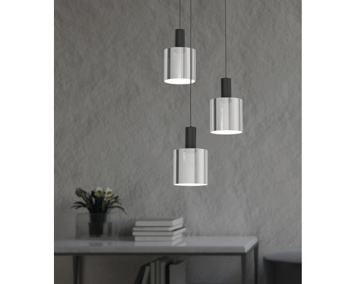 Drie hanglampen met cilindervormige glazen lampenkap hangen boven een tafel.