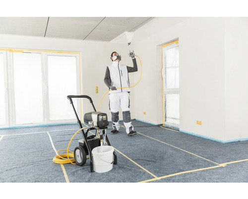 Een man gebruikt een verfspuit in een afgedekte ruimte voor schilderwerk.