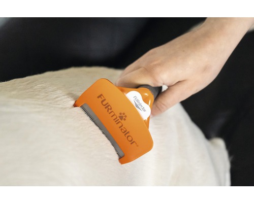 Een hand gebruikt een Furminator-vachtborstel op de vacht van een dier.