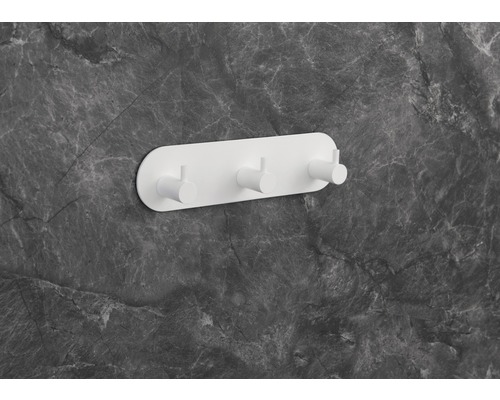 Witte wandkapstok met drie haken aan een grijze marmeren muur.