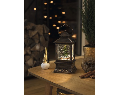 Decoratieve scène met een sneeuwbollantaarn, een kabouterfiguur en een kamerplant op een tafel