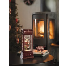 Decoratieve sneeuwbol in de vorm van een telefooncel met kerstmanmotief en open haard op de achtergrond.