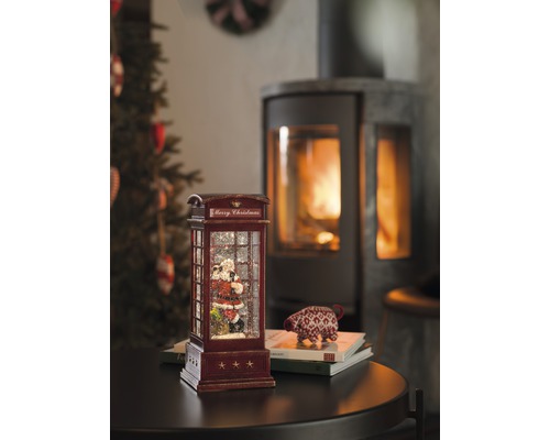 Decoratieve sneeuwbol in de vorm van een telefooncel met kerstmanmotief en open haard op de achtergrond.