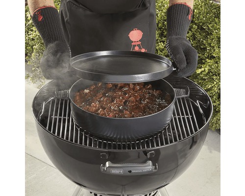 Persoon bereidt gerecht in een Dutch Oven op een kogelbarbecue.