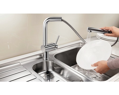 Roestvrijstalen gootsteen met verchroomde kraan en handdouche tijdens het afwassen van een bord