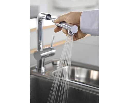 Hand houdt keukenkraan met sproeier boven gootsteen