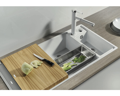 Spoelbak met snijplank, afdruipbak en kraan in een lichte keukenomgeving.