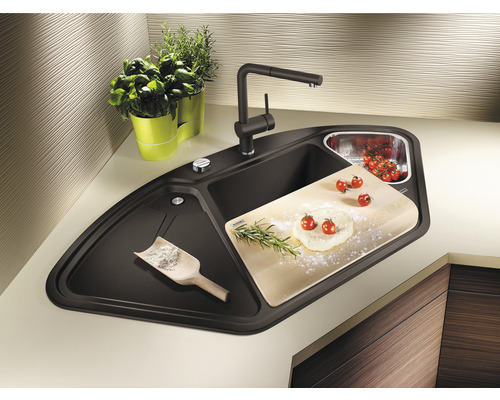 Hoekspoelbak met kraan, snijplank, kruiden en etenswaren op een aanrecht.