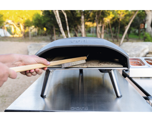 Ooni Logo. Een pizzaborstel wordt in een pizzaoven schoongemaakt.