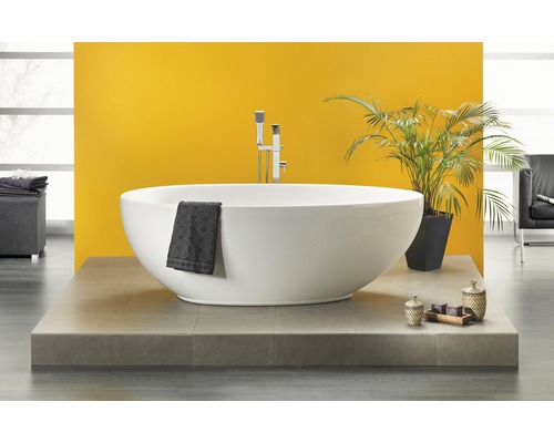 Vrijstaand bad met kraan, handdoek en decoratie op een platform voor een gele muur