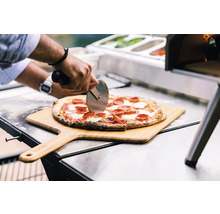 Een pizza wordt op een houten schuif met een pizzasnijder gesneden.