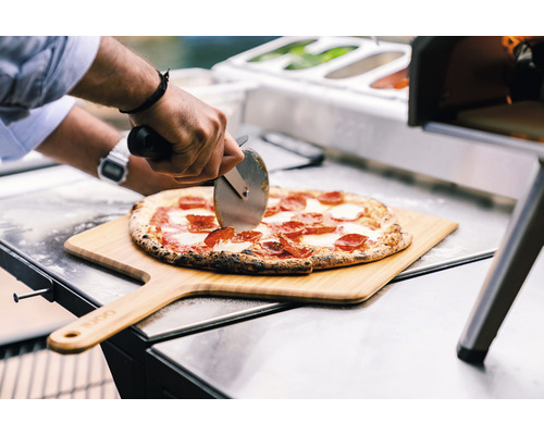 Een pizza wordt op een houten schuif met een pizzasnijder gesneden.