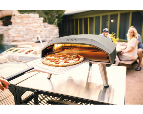 Ooni pizzaoven met pizza op pizzaschep buitenshuis