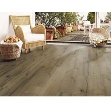 Woonkamer met laminaatvloer in houtlook, rotan stoel en terras met planten.