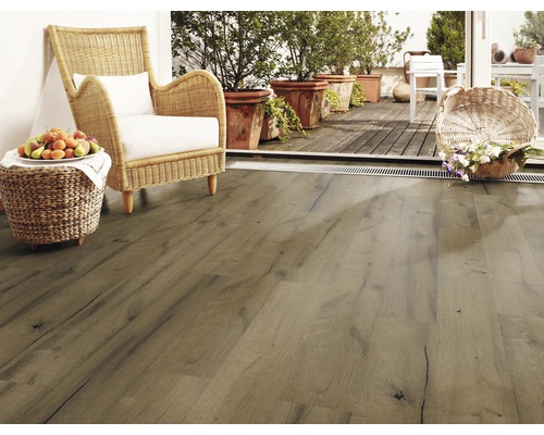 Woonkamer met laminaatvloer in houtlook, rotan stoel en terras met planten.