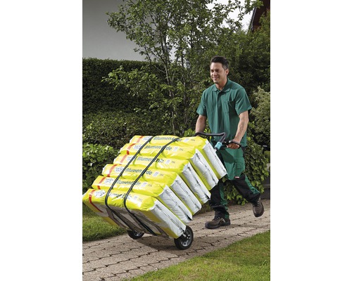 Een persoon duwt met een steekwagen potgrond door een tuin.