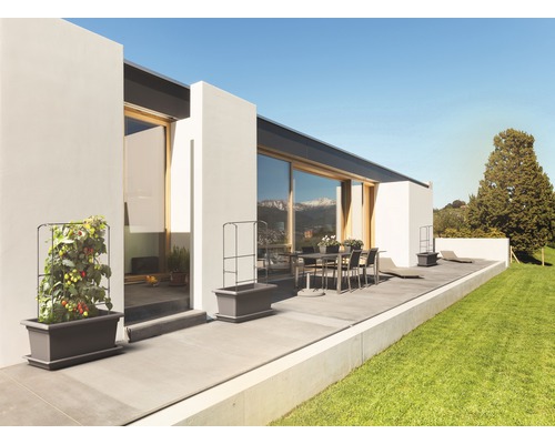 Terras met modern huis, eettafel en beplante plantenbakken met klimrek