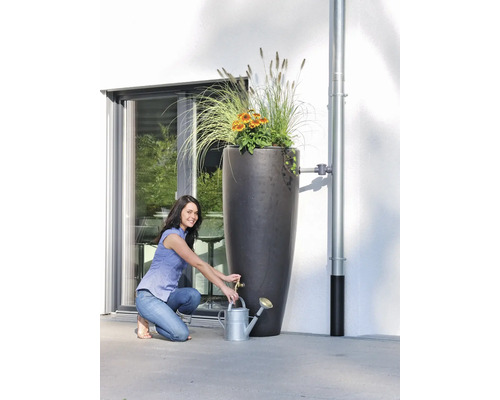 Vrouw vult een gieter bij een hoge regentonzuil met beplanting.