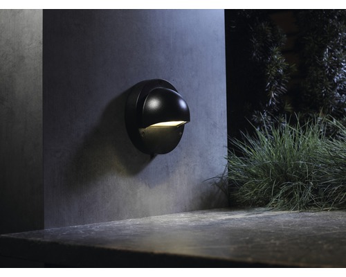 Een zwarte wandlamp is aan een muur bevestigd en verlicht een buitenruimte.