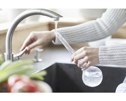 Vrouw vult een glazen fles met water bij de kraan