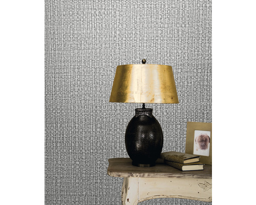 Close-up van een zilverkleurig textielbehang dat textielstructuur imiteert, met een lamp op een tafel