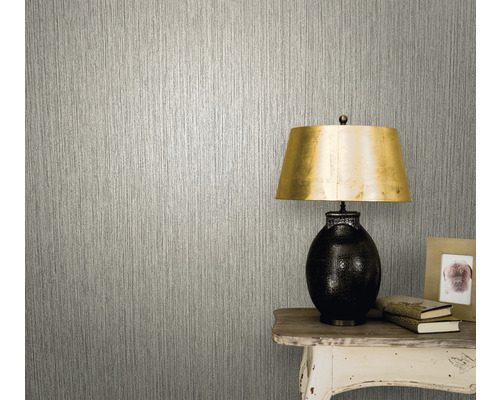 Close-up van een muur met een behang met een verticaal structuureffect naast een tafel met een lamp, boeken en een fotolijst.