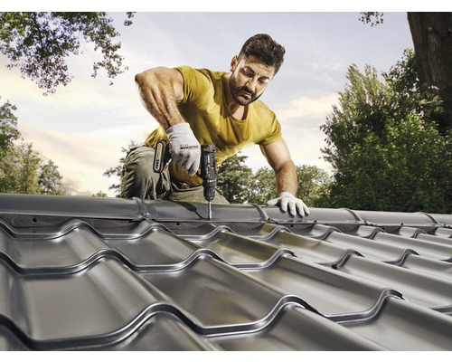 Een man bevestigt metalen dakpannen met een accuschroevendraaier op een dak.
