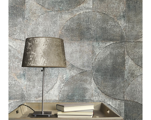 Gedetailleerde opname van een grijze kamerwand met cirkelvormig behangpatroon, een tafel met een lamp en boeken.