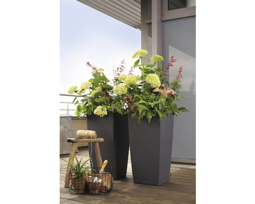 Twee hoge plantenbakken met bloemen en planten op een houten vloer.