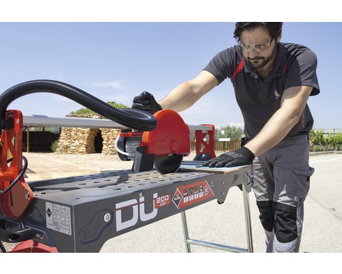 Een man bedient een Rubi tegelsnijmachine om tegels te snijden.