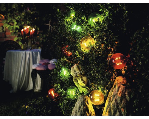 Versierde tuin met verlichte bollen en een sculptuur in de struiken