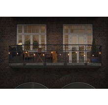 Gedecoreerd balkon met lichtsnoer, stoelen, tafel en planten voor een bakstenen gebouw.