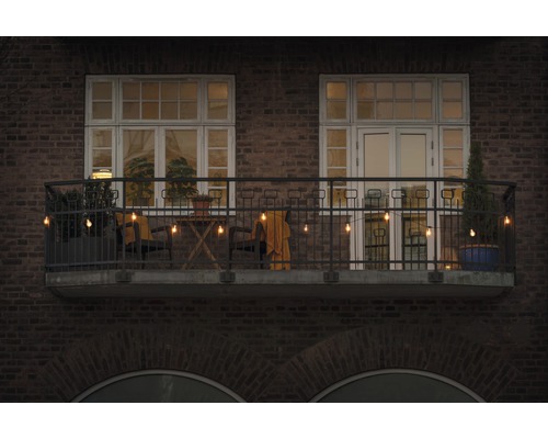 Gedecoreerd balkon met lichtsnoer, stoelen, tafel en planten voor een bakstenen gebouw.