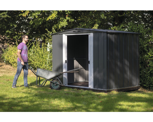 Tuinscene met metalen tuinhuis en een persoon die een kruiwagen duwt