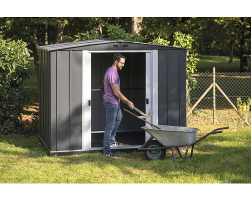 Metalen tuinhuis met man, kruiwagen en tuingereedschap in de tuin