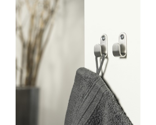 Twee metalen handdoekhaken zijn aan een muur bevestigd, aan één hangt een handdoek.