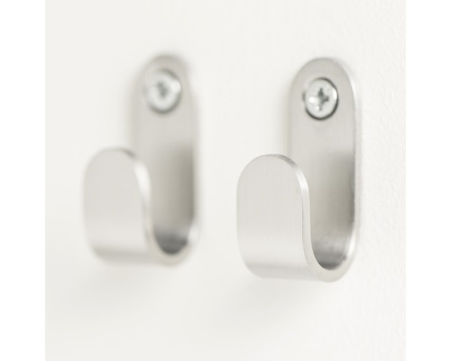 Twee zilverkleurige metalen kapstokhaken met schroeven bevestigd aan een wand.