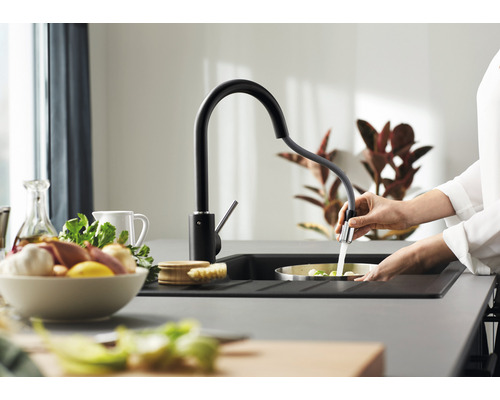 Iemand spoelt groenten in een gootsteen met een zwarte keukenkraan.